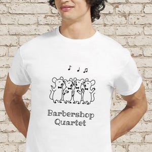 Puede incluir: Camiseta blanca con una ilustración en blanco y negro de cuatro ratones con pajaritas cantando, con notas musicales encima. El texto "Barbershop Quartet" está impreso debajo en una fuente estilizada.