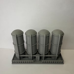 Könnte beinhalten: Graues Modell von vier industriellen Lagertanks mit abgerundeten Deckeln, die durch Rohre verbunden und auf einer rechteckigen Basis montiert sind. Die zylindrischen Tanks haben ein detailliertes Design.
