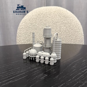 May include: A gray model of an industrial complex, featuring various tanks, towers, and piping. The model includes the text "GRAHAM'S MODELS" with a train logo. The complex is set on a dark surface.