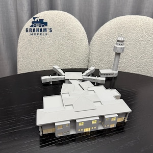 Puede incluir: Maqueta gris de una terminal de aeropuerto con una torre de control y pasarelas. El modelo tiene ventanas y tejados detallados. El logotipo de Graham's Models está en la esquina superior izquierda.