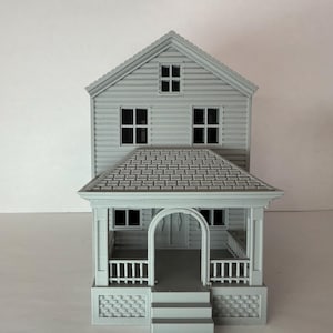 Könnte beinhalten: Ein hellgraues Modellhaus mit zweistöckigem Design. Das Haus verfügt über eine Veranda mit einem bogenförmigen Eingang, mehreren Fenstern und einem Satteldach. Das Modell beinhaltet eine Treppe zur Veranda.