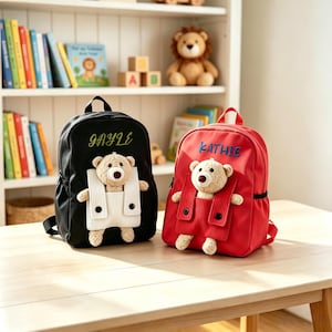 Peut inclure: Deux sacs à dos pour enfants, un noir et un rouge, chacun avec un motif d'ours en peluche. Le sac à dos noir porte le nom "GAYLE" brodé en vert, tandis que le sac à dos rouge porte "KATHIE" en bleu.