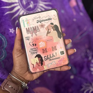 May include: Clear phone case with a pink and white design featuring the word "MAMA" and other phrases like "Mamacita", "Mommy", and "You're doing great". The case also includes illustrations of a mother and child, hearts, and flowers.