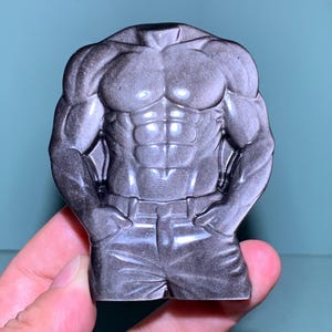 Peut inclure: Figurine de torse sculpté gris avec des muscles définis, les mains dans les poches et une ceinture. La figurine est d'une couleur unie avec des ombres pour accentuer la forme. C'est un objet de fantaisie.