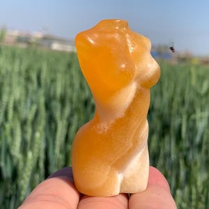 Peut inclure: Une petite sculpture de torse féminin sculptée à la main en calcite orange. La sculpture est lisse et polie, avec une forme naturelle et organique.