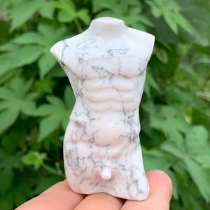 Peut inclure: Une sculpture en marbre blanc d'un torse masculin. La sculpture présente une musculature détaillée et est veinée de gris. La figurine est posée avec les bras et les jambes coupés, et la sculpture est tenue dans une main.