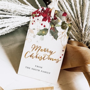 May include: A rectangular Christmas gift tag with a floral design featuring red poinsettias, green leaves, and gold accents. The tag reads "Merry Christmas" in gold script, with "From The Smith Family" below.