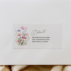 May include: A white envelope featuring a rectangular address label with a watercolor wildflower illustration and the text Deliver to MR & MRS WILLIAM MARKS 4566 HOWARD MILL ROAD WEST HAVEN, GA 305XX, accompanied by a matching return address label.