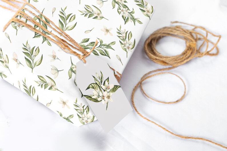 May include: A white gift box with a floral pattern of green leaves and white flowers. The box is tied with twine and has a white gift tag with a floral design.