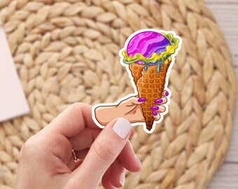 May include: A hand holding a sticker of a melting ice cream cone with purple, blue, and yellow ice cream. The cone is a waffle cone with a yellow drip.
