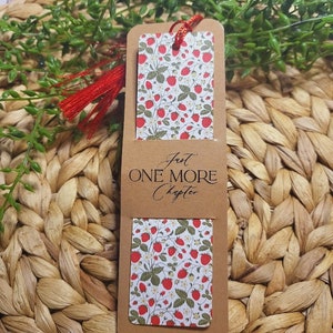 May include: A brown bookmark with a red tassel. The bookmark has a white background with a red strawberry pattern and the text "Just One More Chapter".