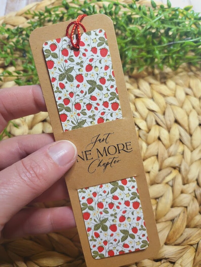May include: A bookmark with a strawberry pattern and the text "Just One More Chapter" on a brown background.