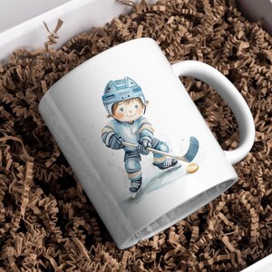 May include: White ceramic mug with a watercolor illustration of a hockey player wearing a blue helmet and jersey. The player is holding a hockey stick and puck.