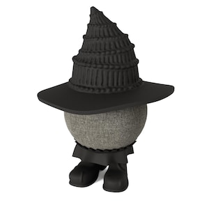 May include: A whimsical figure with a gray, textured sphere for a head, wearing a black witch's hat and matching boots. The hat has a tiered design. A black skirt-like garment is visible. The figure is set against a white background.