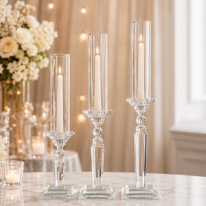 Peut inclure: Trois bougeoirs en verre transparent de hauteurs différentes, chacun doté d'une base carrée, d'un pied à facettes et d'un abat-jour cylindrique en verre. Chaque bougeoir contient une bougie effilée blanche avec une flamme allumée.
