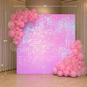 May include: A square pink sequin shimmer wall backdrop measuring 8 feet by 8 feet, decorated with clusters of pink and clear balloons in varying sizes attached to the top left and bottom right corners of the panel structure.