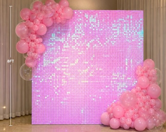 May include: A square pink sequin shimmer wall backdrop measuring 2.44 metres by 2.44 metres, decorated with clusters of pink and clear balloons in varying sizes attached to the top left and bottom right corners of the panel structure.