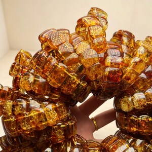 May include: A collection of amber bracelets. Each bracelet is composed of numerous, irregularly shaped, translucent amber beads. The beads vary in shades of golden brown and orange, with visible internal patterns. The bracelets are displayed in a close-up shot, highlighting their texture and color.