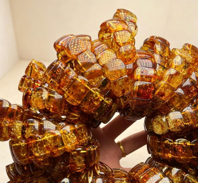 May include: A collection of amber bracelets. Each bracelet is composed of numerous, irregularly shaped, translucent amber beads. The beads vary in shades of golden brown and orange, with visible internal patterns. The bracelets are displayed in a close-up shot, highlighting their texture and color.