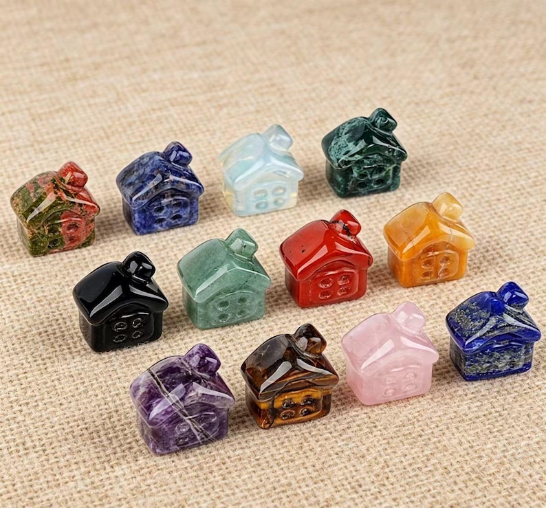 May include: A collection of small, gemstone house figurines in various colors, including green, red, and blue. Each house has a chimney and windows, and they are arranged on a neutral-toned surface.