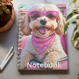 May include: A spiral-bound notebook with a cartoon dog wearing pink sunglasses and a pink bandana. The dog is set against a pink car interior. The word "Notebook" is printed in white on the cover.