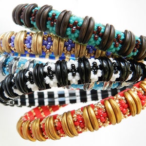 Peut inclure: Cinq bracelets en perles color&eacute;es empil&eacute;s les uns sur les autres. Les bracelets sont faits de perles de diff&eacute;rentes couleurs et motifs, notamment noir et blanc, rouge et or, et bleu et marron.