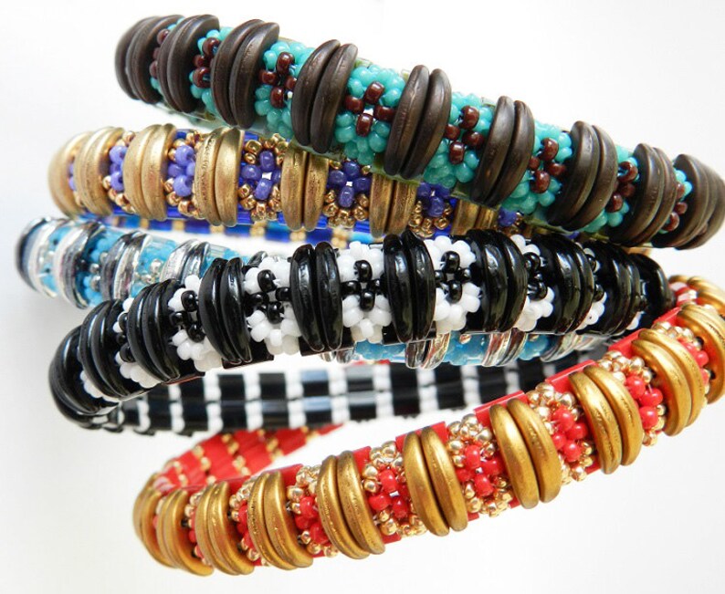 Peut inclure: Cinq bracelets en perles color&eacute;es empil&eacute;s les uns sur les autres. Les bracelets sont faits de perles de diff&eacute;rentes couleurs et motifs, notamment noir et blanc, rouge et or, et bleu et marron.