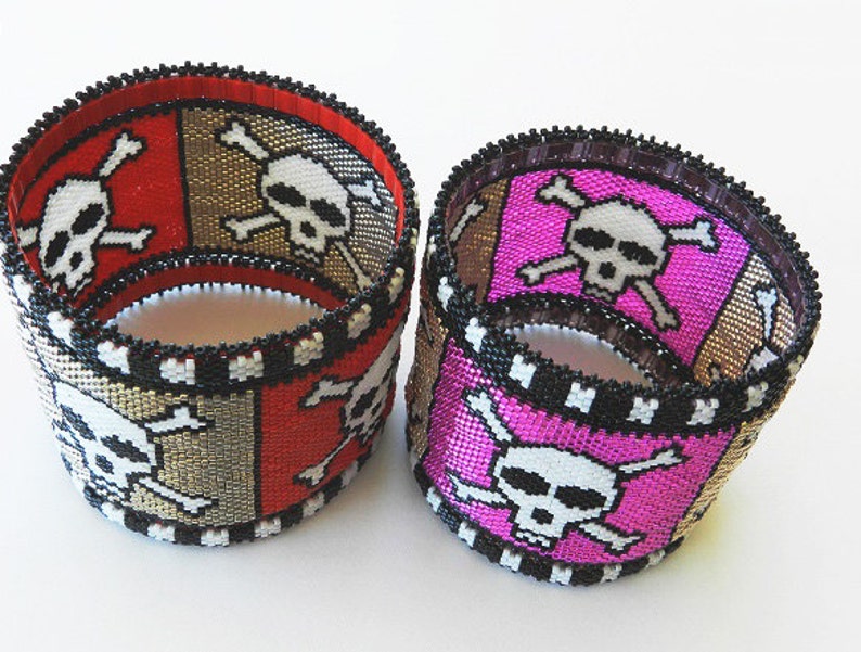 Puede incluir: Dos pulseras de cuentas con un dise&ntilde;o de calavera y huesos cruzados. Una pulsera es roja, dorada y negra, y la otra es rosa, dorada y negra.