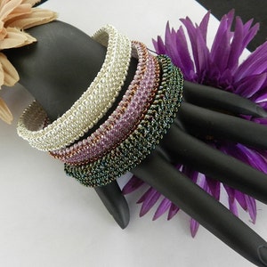 May include: Four beaded bracelets stacked on a black hand model. The bracelets are made of silver, pink, copper, and green beads.