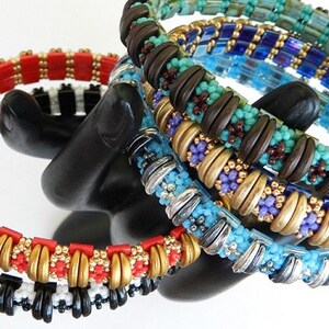 Peut inclure: Un ensemble de six bracelets en perles de diff&eacute;rentes couleurs, dont le rouge, le noir, le blanc, l'or, le turquoise, le marron et le violet. Les bracelets sont empil&eacute;s sur un support noir.