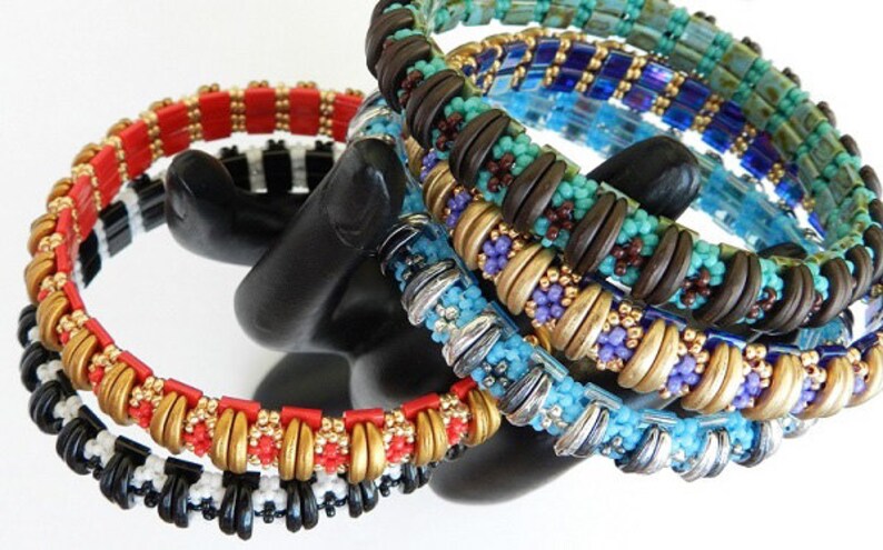 Peut inclure: Un ensemble de six bracelets en perles de diff&eacute;rentes couleurs, dont le rouge, le noir, le blanc, l'or, le turquoise, le marron et le violet. Les bracelets sont empil&eacute;s sur un support noir.