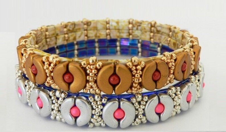 K&ouml;nnte beinhalten: Drei Perlenarmb&auml;nder, die &uuml;bereinander gestapelt sind. Das obere Armband ist goldfarben mit roten Perlen, das mittlere Armband ist blau mit schillernden Perlen und das untere Armband ist silberfarben mit rosa Perlen.