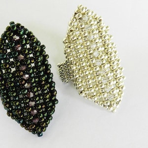 May include: Two beaded rings, one green and one silver, shaped like a leaf. The rings are made of small beads and have a textured surface.