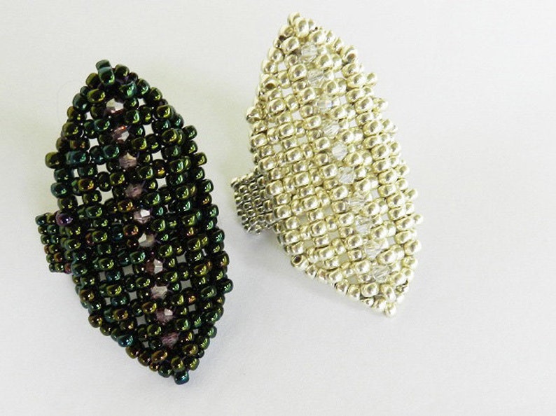 May include: Two beaded rings, one green and one silver, shaped like a leaf. The rings are made of small beads and have a textured surface.