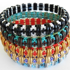 Peut inclure: Cinq bracelets en perles empil&eacute;s les uns sur les autres. Le bracelet du haut est noir et blanc, le deuxi&egrave;me est brun et turquoise, le troisi&egrave;me est or et rouge, le quatri&egrave;me est violet et or, et le bracelet du bas est bleu et argent.