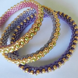 May include: Three beaded bracelets in shades of purple, green, and pink. The bracelets are made with small, round beads and are stacked on top of each other.