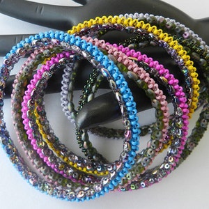 May include: A set of eight beaded bracelets in various colors, including blue, pink, yellow, and green. The bracelets are made with small, iridescent beads and are stacked on top of each other.