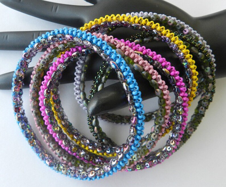 May include: A set of eight beaded bracelets in various colors, including blue, pink, yellow, and green. The bracelets are made with small, iridescent beads and are stacked on top of each other.