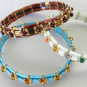 May include: Three beaded bracelets in different colors and styles. The top bracelet is brown with gold accents and iridescent beads. The middle bracelet is white with silver beads and a few colorful beads. The bottom bracelet is light blue with gold beads and clear crystals.