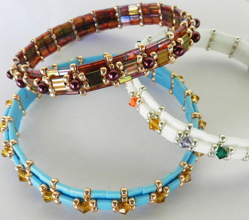 May include: Three beaded bracelets in different colors and styles. The top bracelet is brown with gold accents and iridescent beads. The middle bracelet is white with silver beads and a few colorful beads. The bottom bracelet is light blue with gold beads and clear crystals.