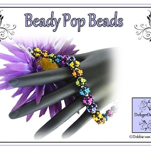 May include: A colorful beaded bracelet with black, yellow, green, pink, and blue beads. The bracelet is on a black hand model and a purple flower.
