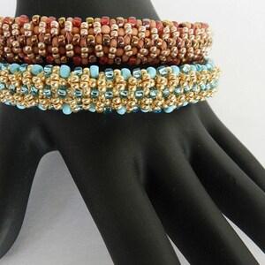 Puede incluir: Tres pulseras de cuentas apiladas en un maniqu&iacute; de mano negro. La pulsera superior es marr&oacute;n y dorada, la pulsera del medio es dorada y azul, y la pulsera inferior es dorada y azul.