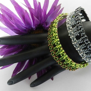 Puede incluir: Tres pulseras de cuentas en un maniqu&iacute; de mano negro. Las pulseras son verdes, marrones y plateadas con cuentas negras. Las pulseras est&aacute;n apiladas unas sobre otras.