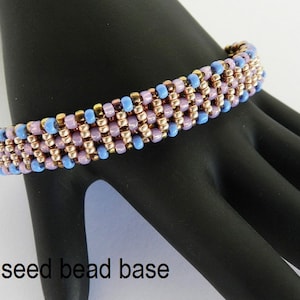 Puede incluir: Un primer plano de un brazalete de cuentas con una base de cuentas de semillas de tama&ntilde;o 8. El brazalete est&aacute; hecho con cuentas de color azul claro, rosa y cobre.