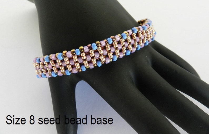 Puede incluir: Un primer plano de un brazalete de cuentas con una base de cuentas de semillas de tama&ntilde;o 8. El brazalete est&aacute; hecho con cuentas de color azul claro, rosa y cobre.