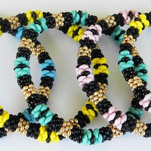 Op de afbeelding: Vijf kleurrijke kralenarmbanden in zwart, geel, turquoise, roze en goud. De armbanden liggen op elkaar.