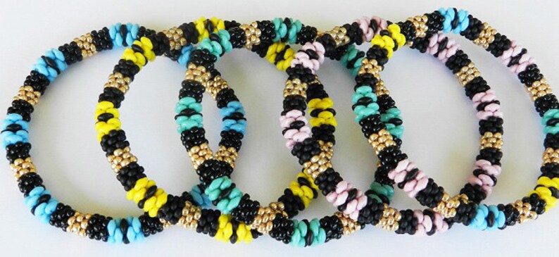 Op de afbeelding: Vijf kleurrijke kralenarmbanden in zwart, geel, turquoise, roze en goud. De armbanden liggen op elkaar.