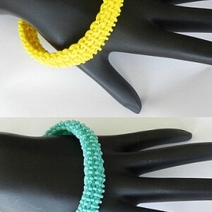 May include: Two beaded bracelets, one yellow and one turquoise, on a black mannequin hand.