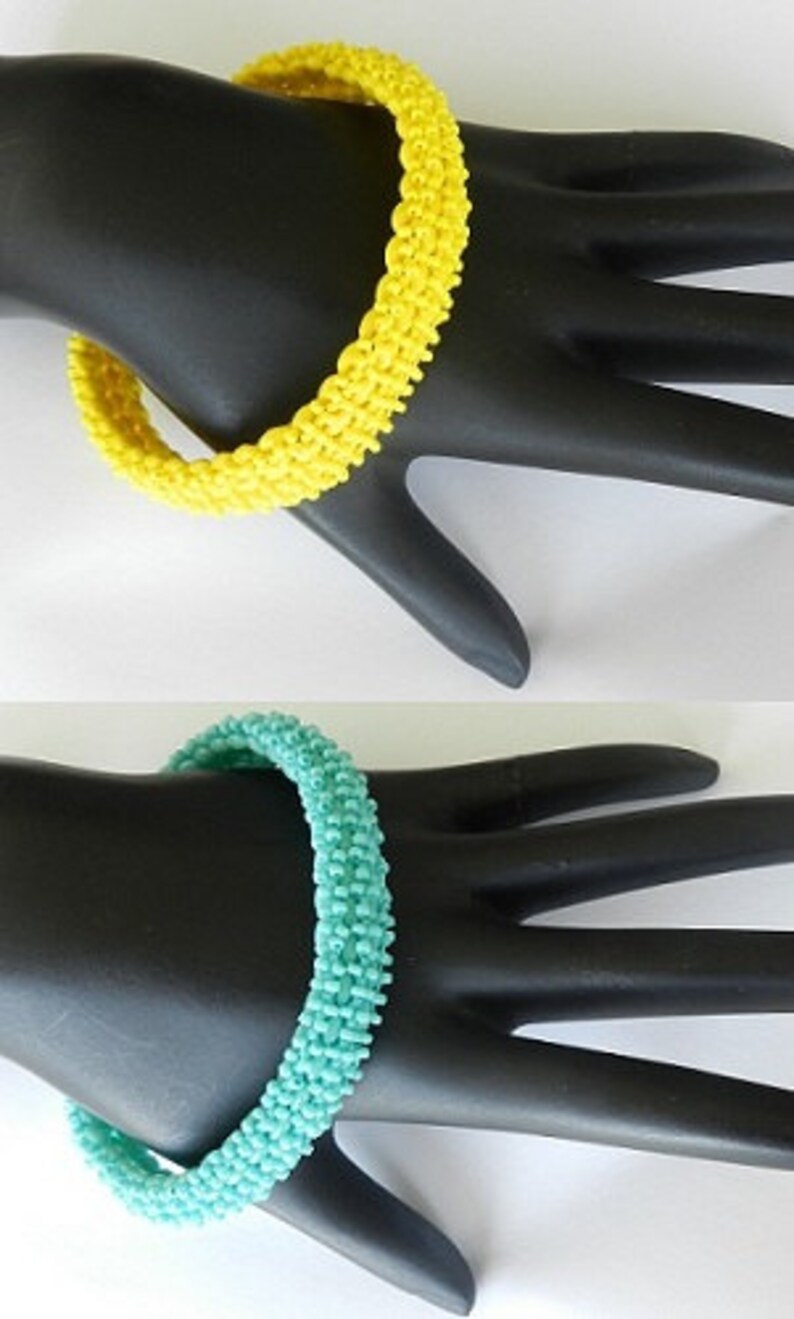 May include: Two beaded bracelets, one yellow and one turquoise, on a black mannequin hand.