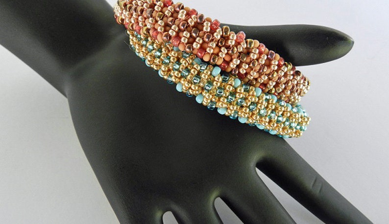 Puede incluir: Tres pulseras de cuentas apiladas en una mano negra. La pulsera superior es roja, naranja y dorada. La pulsera del medio es dorada y turquesa. La pulsera inferior es dorada y turquesa.